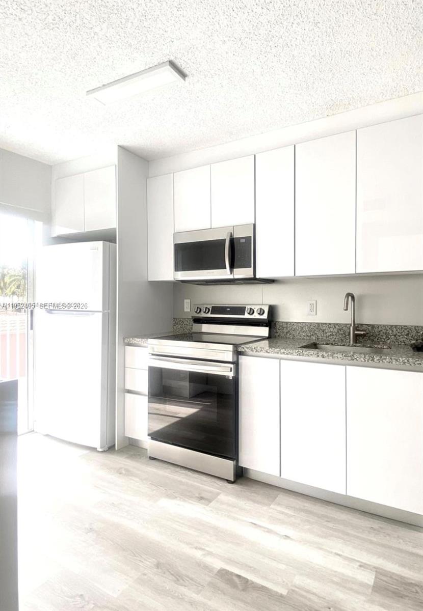 A kitchen features white cabinets, stainless steel appliances, and speckled granite countertops — 2575 SW 27th Ave # 210, Miami FL 33133, MIAMI, FL
