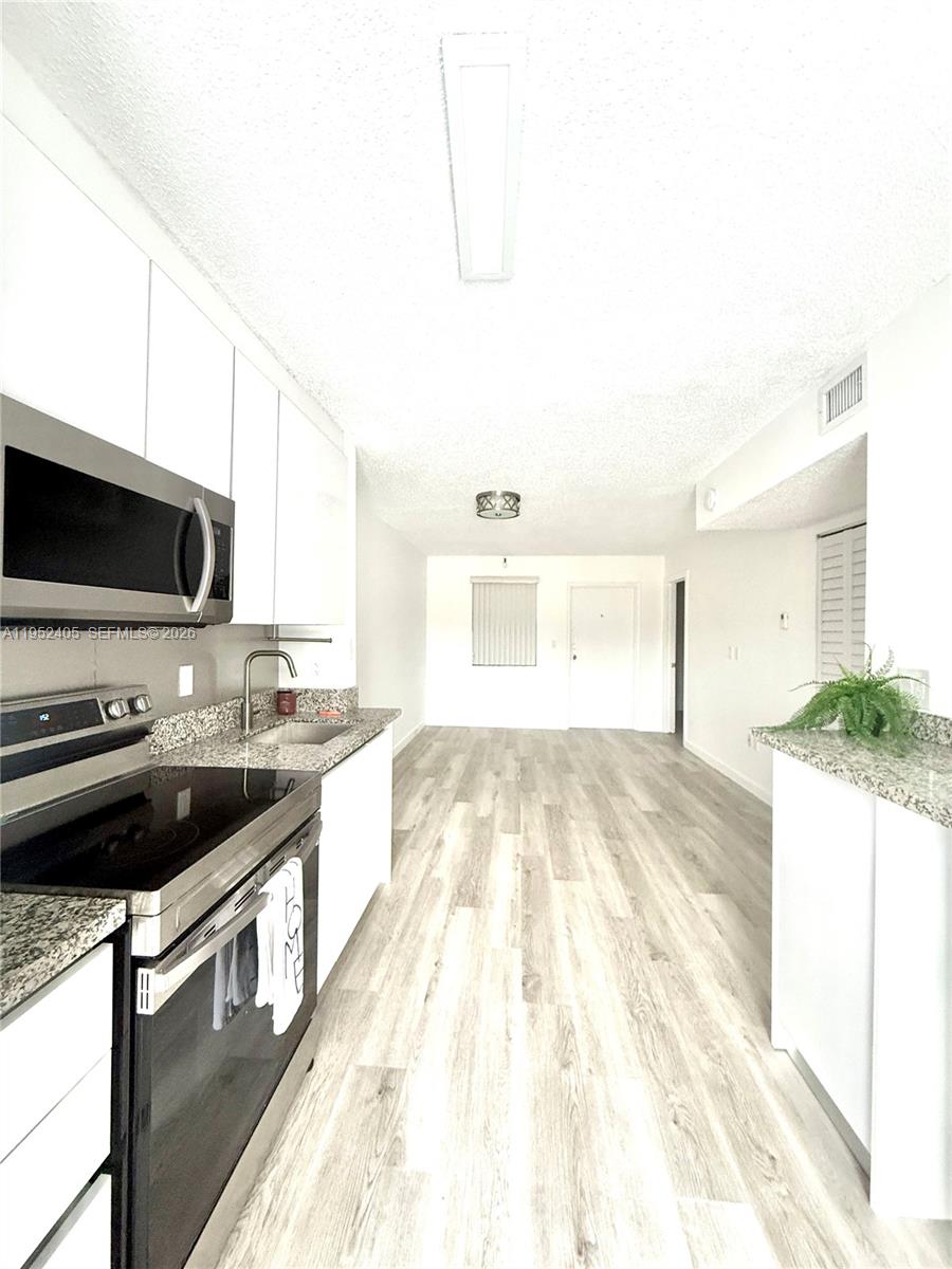 A kitchen with white cabinets, stainless steel appliances, and wood-look flooring leads to an entryway — 2575 SW 27th Ave # 210, Miami FL 33133, MIAMI, FL