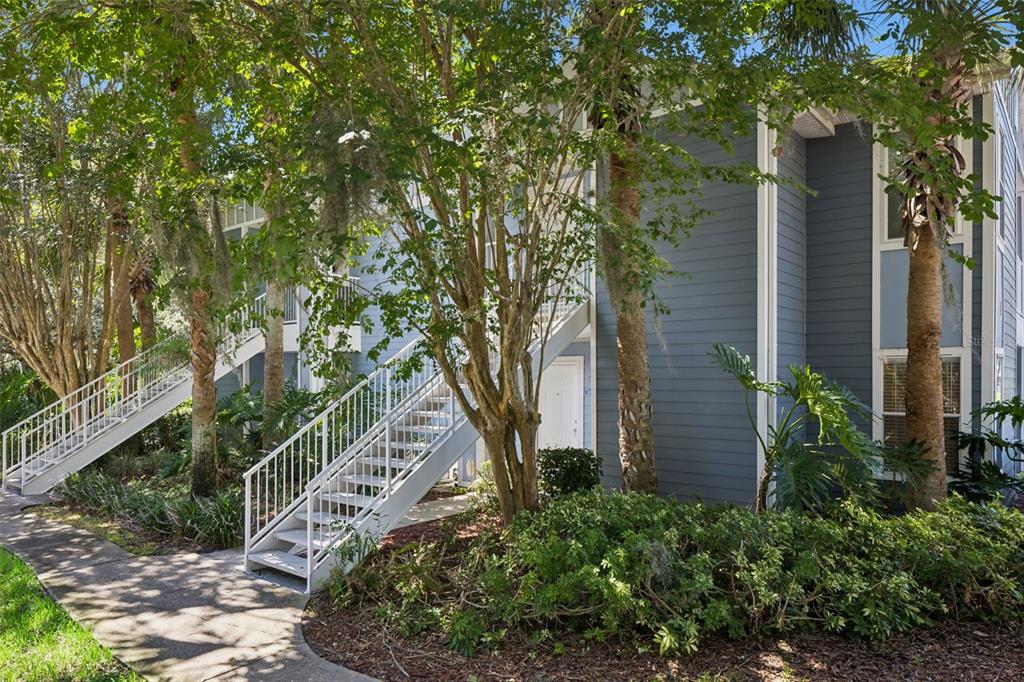An exterior view of a blue multi-story apartment building with white stairs and landscaping — 2532 GRASSY POINT DR UNIT 100, LAKE MARY, FL