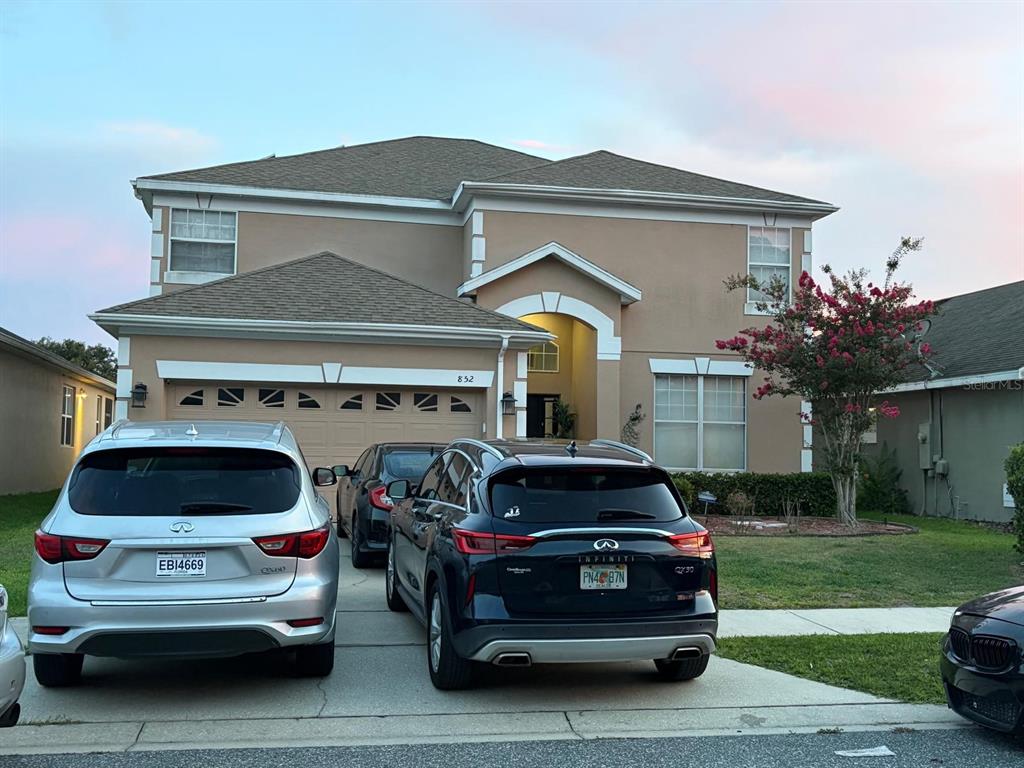 A two-story tan house with a multi-car driveway and several parked vehicles — 852 HARING LANE, MOUNT DORA, FL