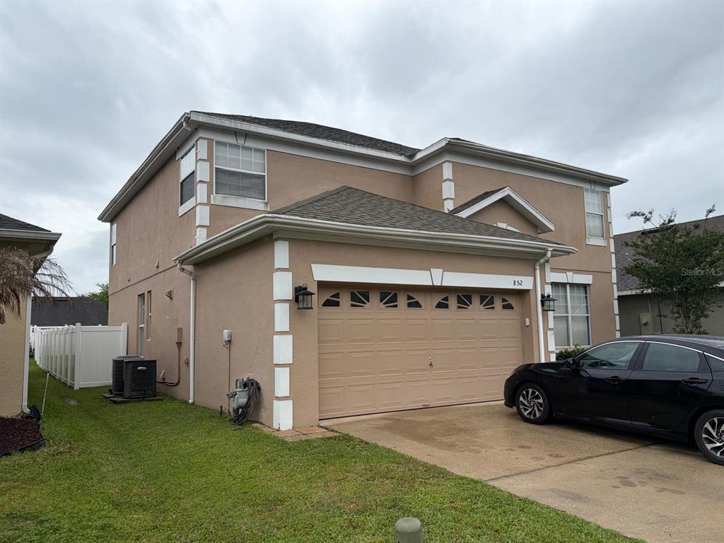 A two-story tan house with white trim and a two-car garage under a cloudy sky — 852 HARING LANE, MOUNT DORA, FL