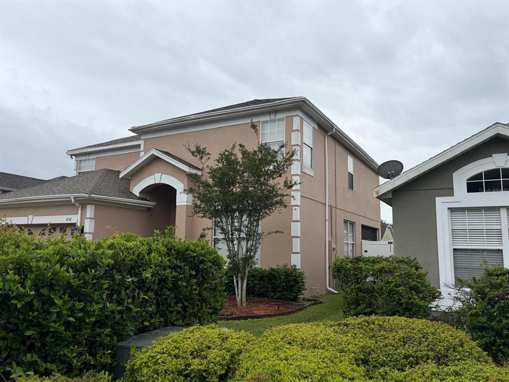A two-story tan stucco house with a side-entry garage and a landscaped front yard — 852 HARING LANE, MOUNT DORA, FL