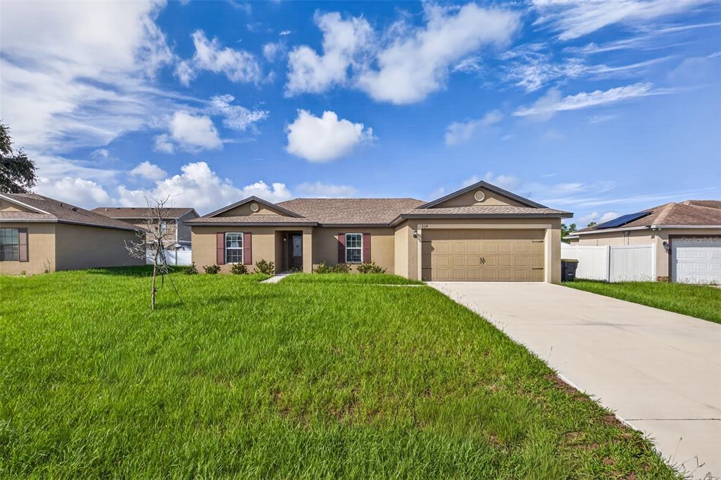 A single-story tan house with a two-car garage and a large front lawn — 334 BEGONIA COURT, POINCIANA, FL