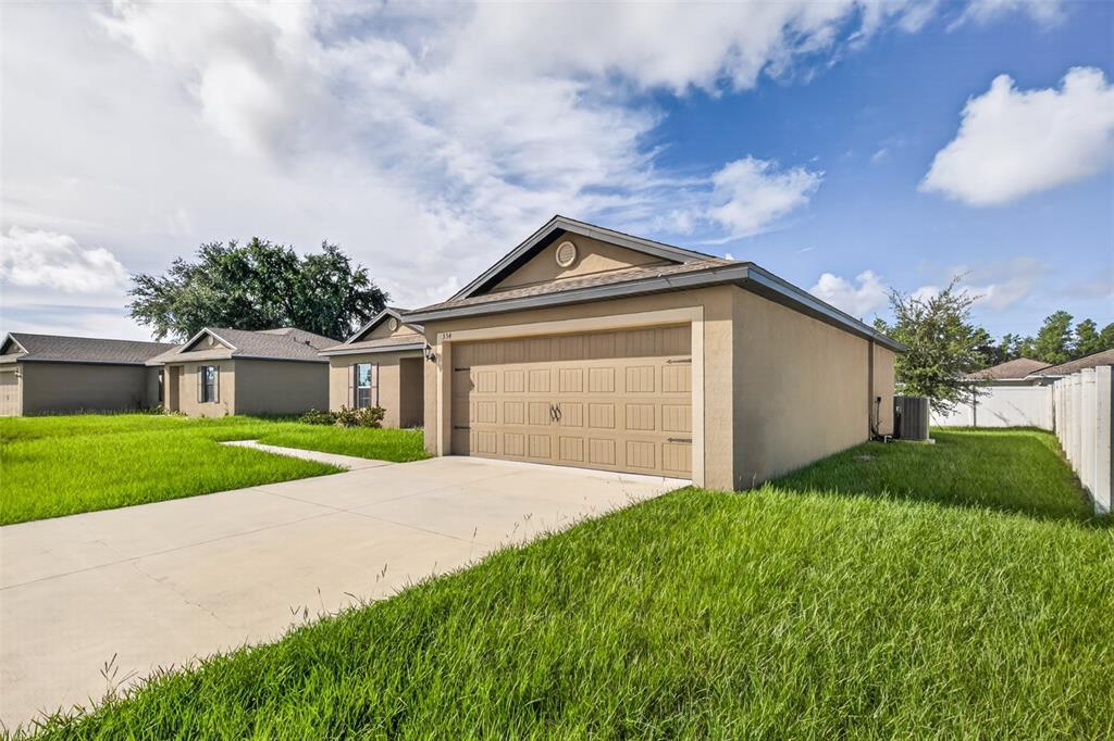 A tan single-story house with a two-car garage and a concrete driveway under a blue sky — 334 BEGONIA COURT, POINCIANA, FL