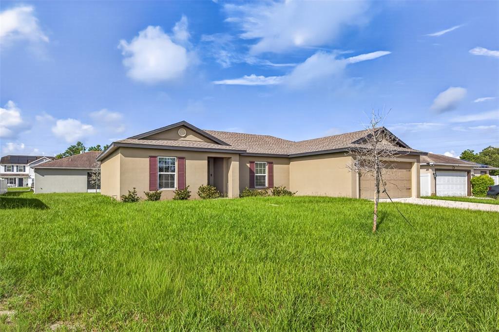 A single-story tan stucco house with a two-car garage and a large grassy front yard — 334 BEGONIA COURT, POINCIANA, FL