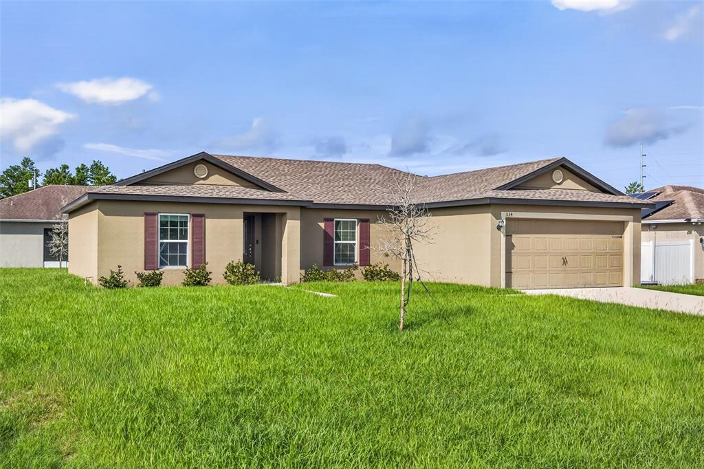 A single-story tan house with a brown shingled roof and a two-car garage — 334 BEGONIA COURT, POINCIANA, FL