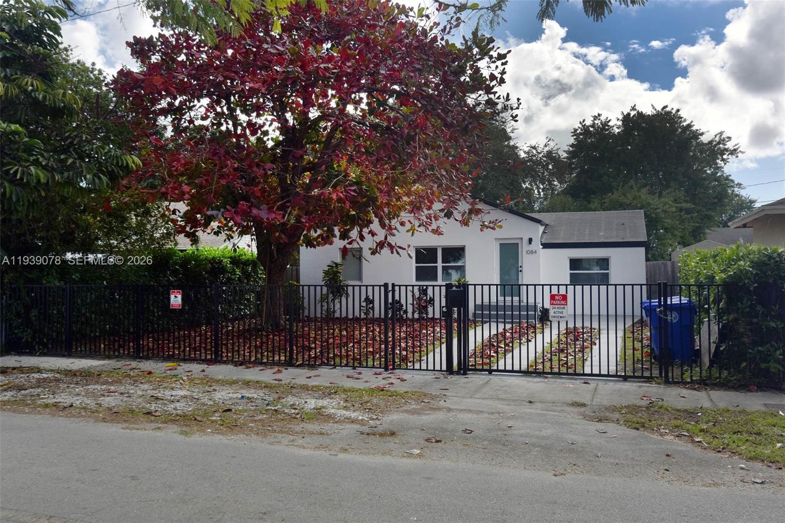 A white single-story house features a black metal fence and a large red-leafed tree — 1084 NW 66th St, Miami FL 33150, MIAMI, FL