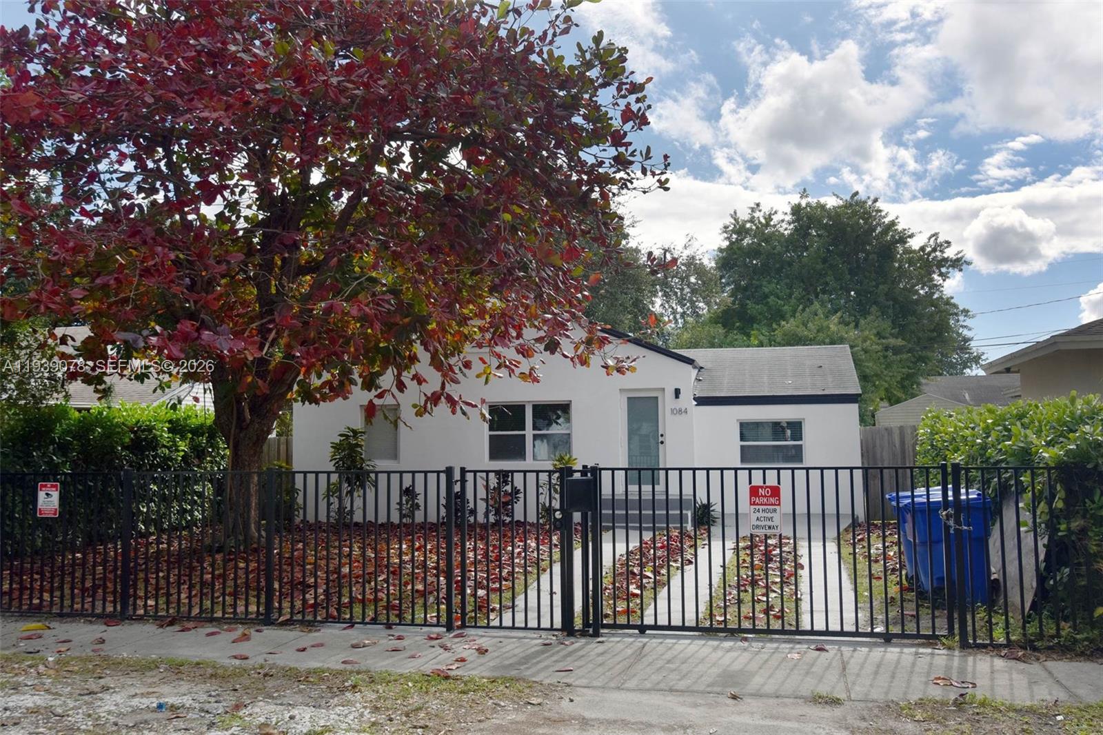 A white single-story house with a black metal fence and a large red-leafed tree — 1084 NW 66th St, Miami FL 33150, MIAMI, FL