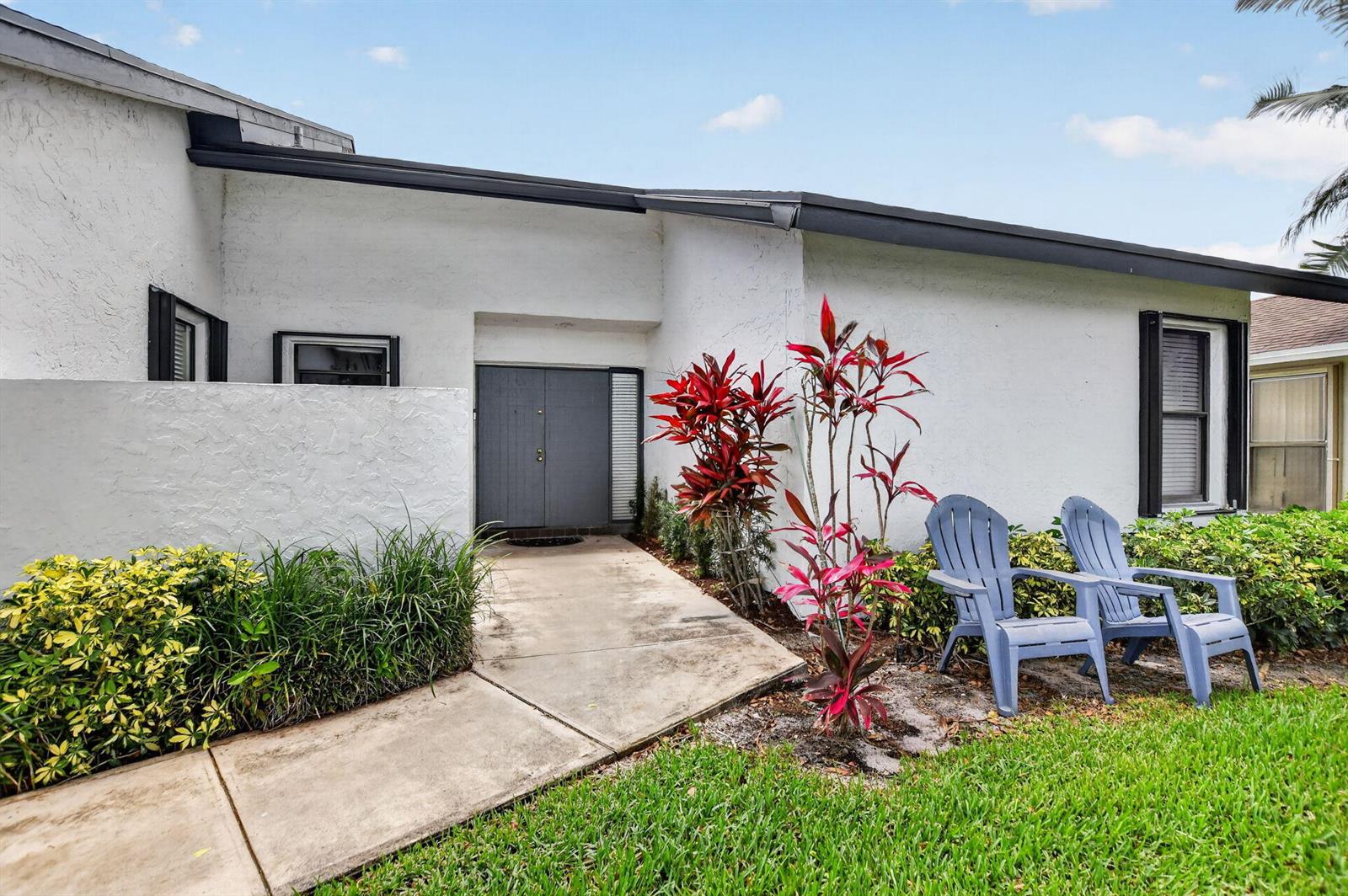 The exterior of a white house features a gray double door and two blue chairs — 7833 San Marcos Place, Boca Raton FL 33433, BOCA RATON, FL