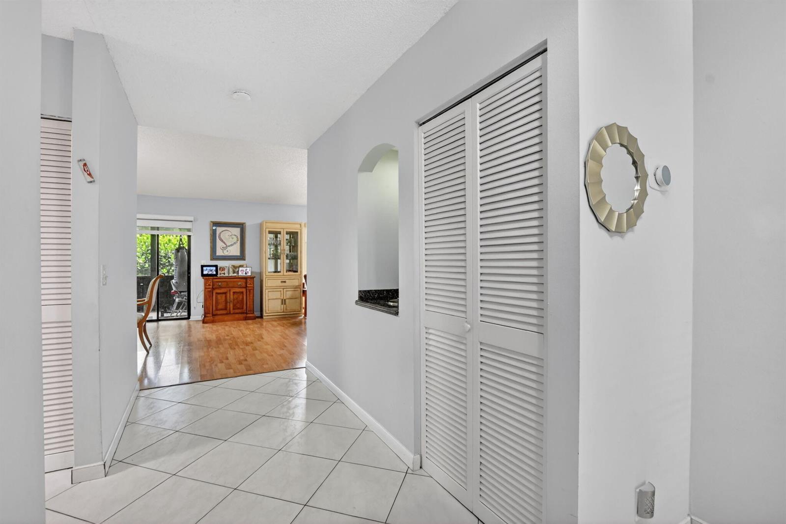 A hallway with white tile flooring leads to a living area with hardwood floors — 7833 San Marcos Place, Boca Raton FL 33433, BOCA RATON, FL