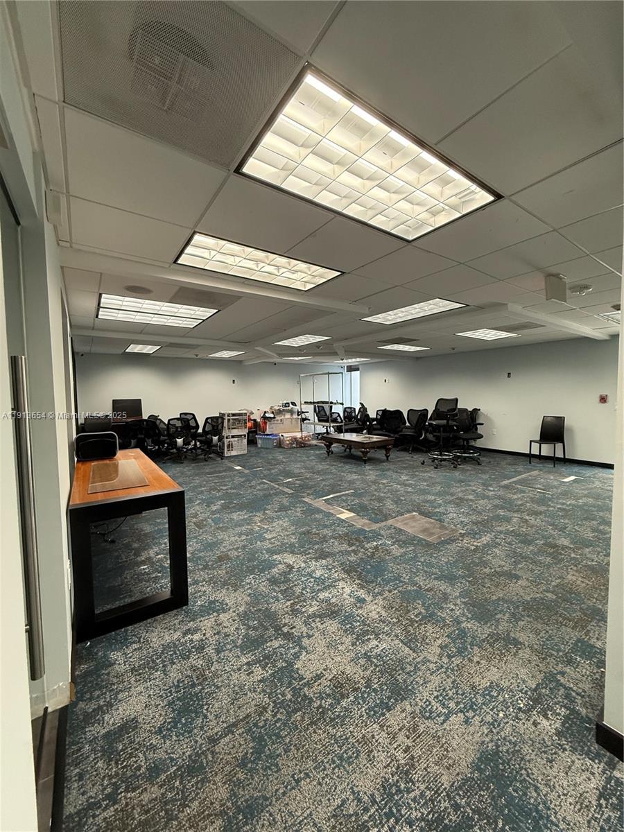 An office space features a patterned blue carpet, drop ceiling with recessed lighting, and scattered chairs — 9450 SW 72nd St, Miami FL 33173, MIAMI, FL