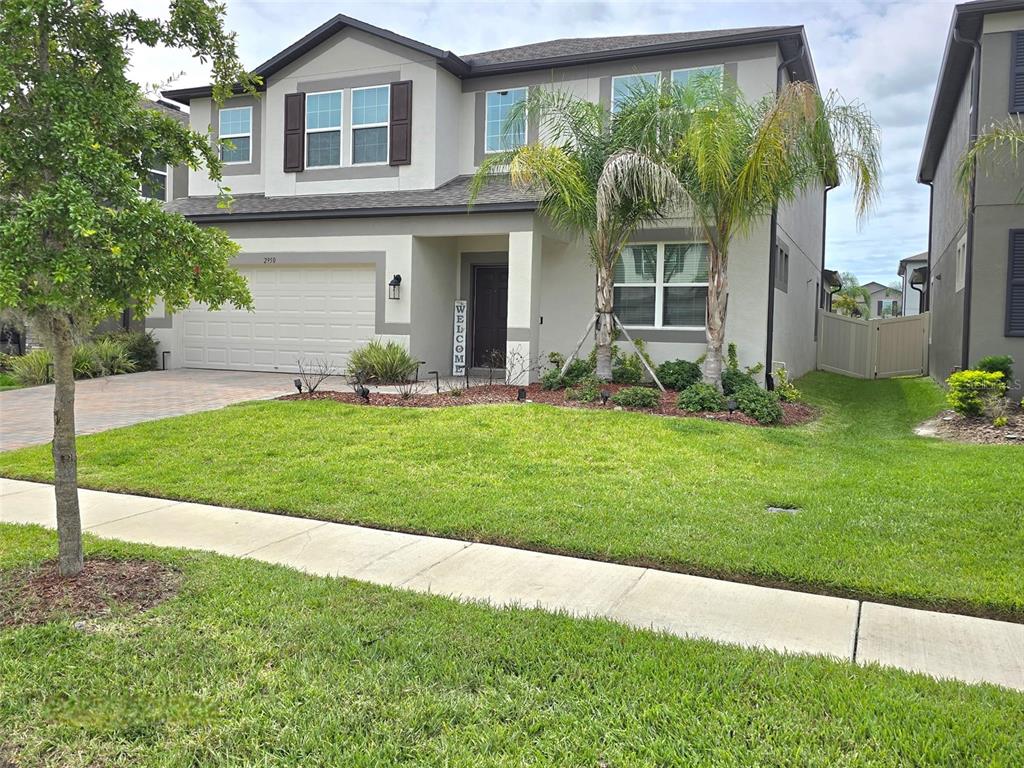 A two-story suburban house with a beige stucco exterior, a two-car garage, and palm trees — 2950 ADAMS CROSS DRIVE, ZEPHYRHILLS, FL