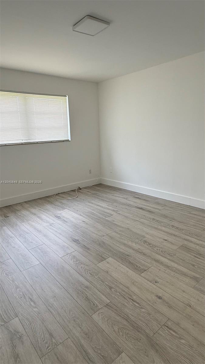 An empty room features light wood-look flooring, white walls, and a window with blinds — 411 SE 10th St # 3, Hallandale Beach FL 33009, HALLANDALE BEACH, FL