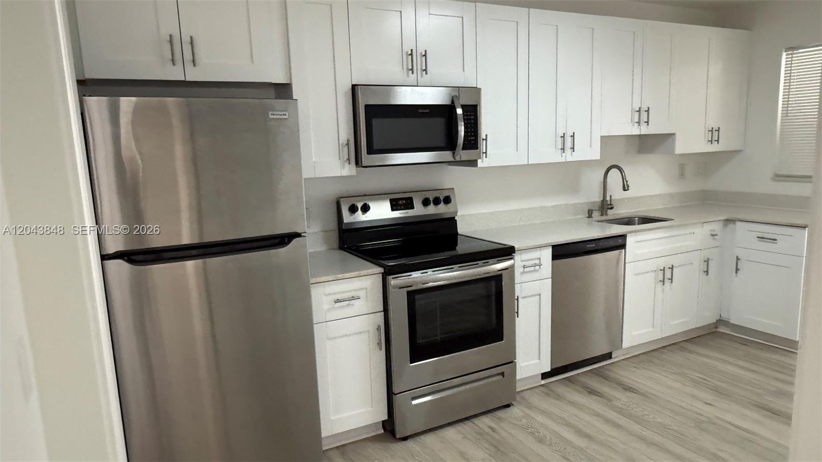 A kitchen features white cabinets, stainless steel appliances, and light-colored wood-look flooring — 411 SE 10th St # 3, Hallandale Beach FL 33009, HALLANDALE BEACH, FL