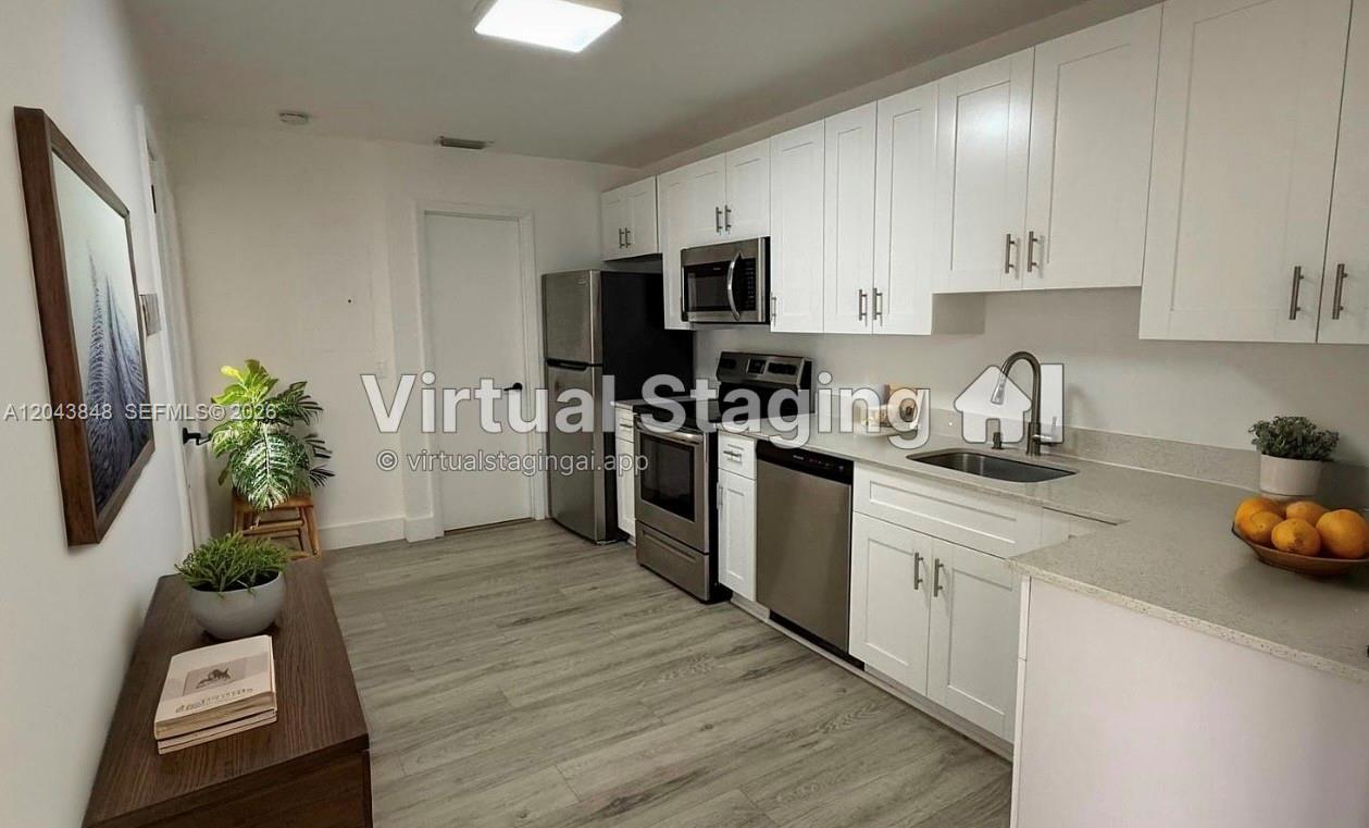 A kitchen features white cabinets, stainless steel appliances, and light-colored wood-look flooring — 411 SE 10th St # 3, Hallandale Beach FL 33009, HALLANDALE BEACH, FL