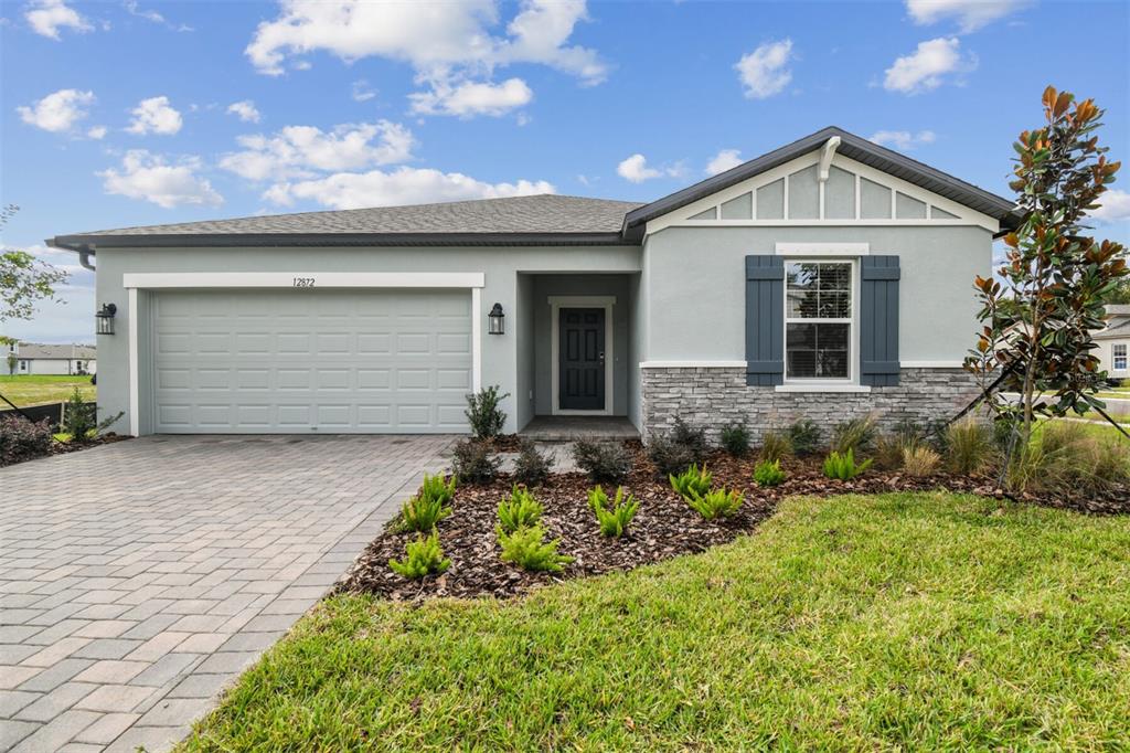 A single-story house with a gray stucco exterior, stone accents, and a paved driveway — 12872 CASTLE OAKS DRIVE, HUDSON, FL