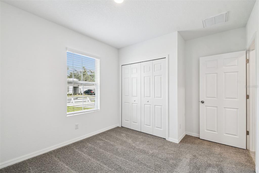 A bedroom with white walls, gray carpet, a window, a closet, and a closed door — 12872 CASTLE OAKS DRIVE, HUDSON, FL
