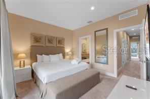 A bedroom features a king bed, a bench, a mirror, and an attached bathroom doorway — 3175 BRASILIA AVENUE, KISSIMMEE, FL