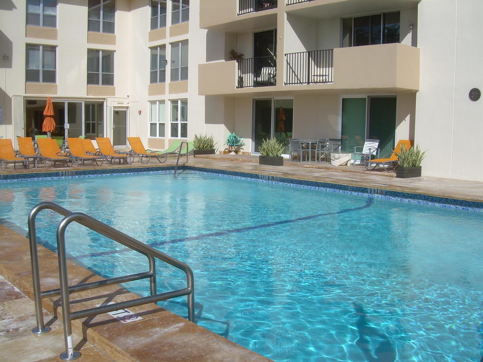 A swimming pool with lounge chairs and patio furniture sits outside a multi-story apartment building — 1000 Spanish River Road # 3b, Boca Raton FL 33432, BOCA RATON, FL