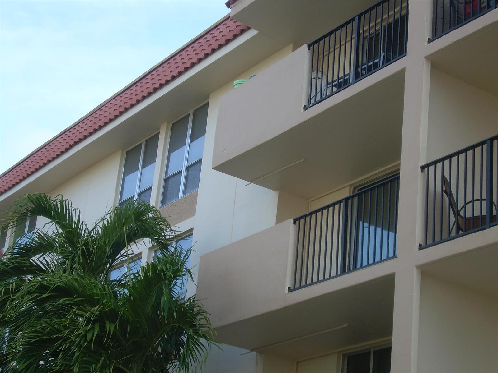 A low-angle view of a multi-story apartment building with balconies and a palm tree — 1000 Spanish River Road # 3b, Boca Raton FL 33432, BOCA RATON, FL