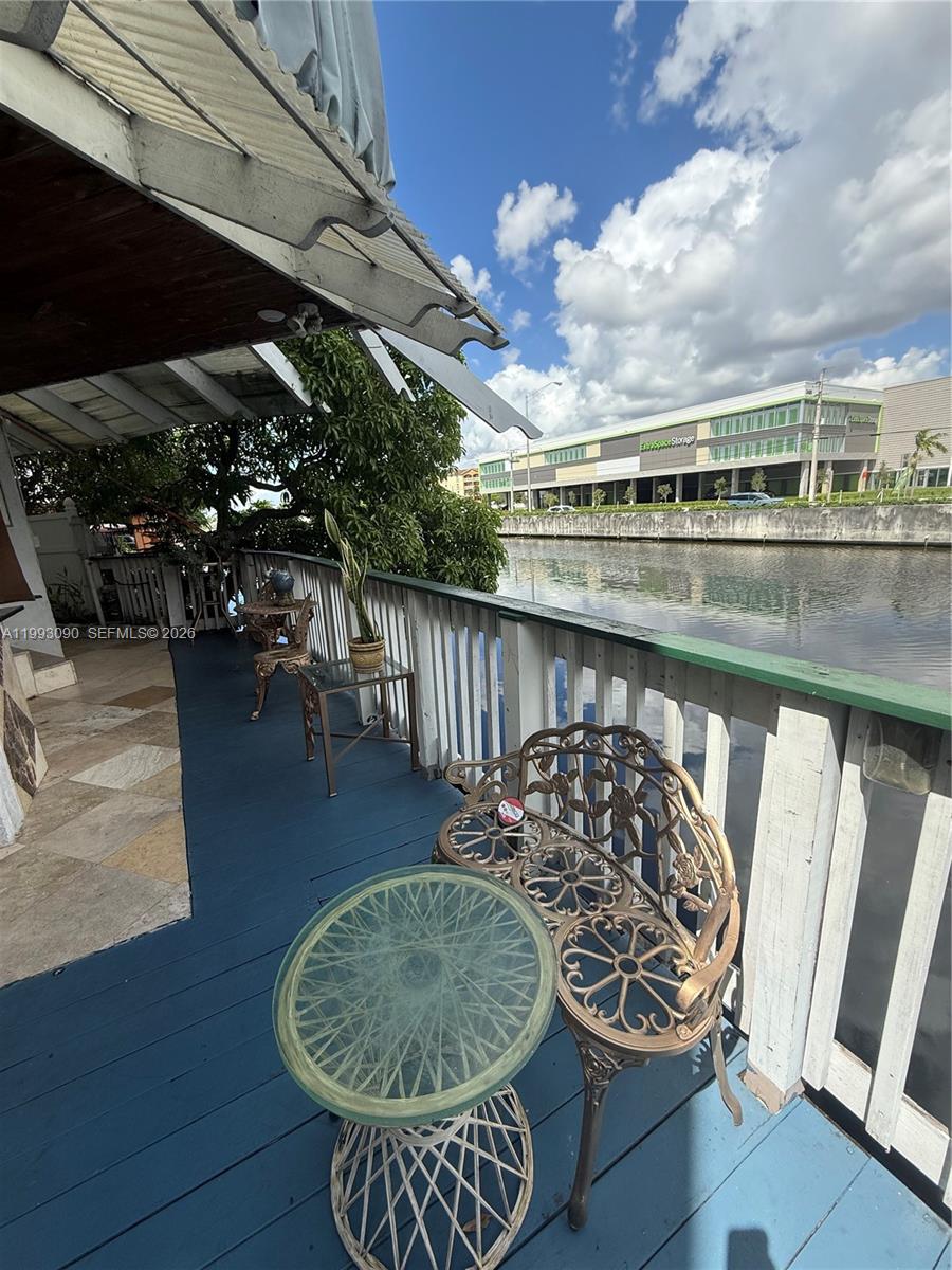 A blue-painted wooden deck overlooks a canal with a large storage building in the background — 7643 NW South River Dr, Medley FL 33166, MEDLEY, FL