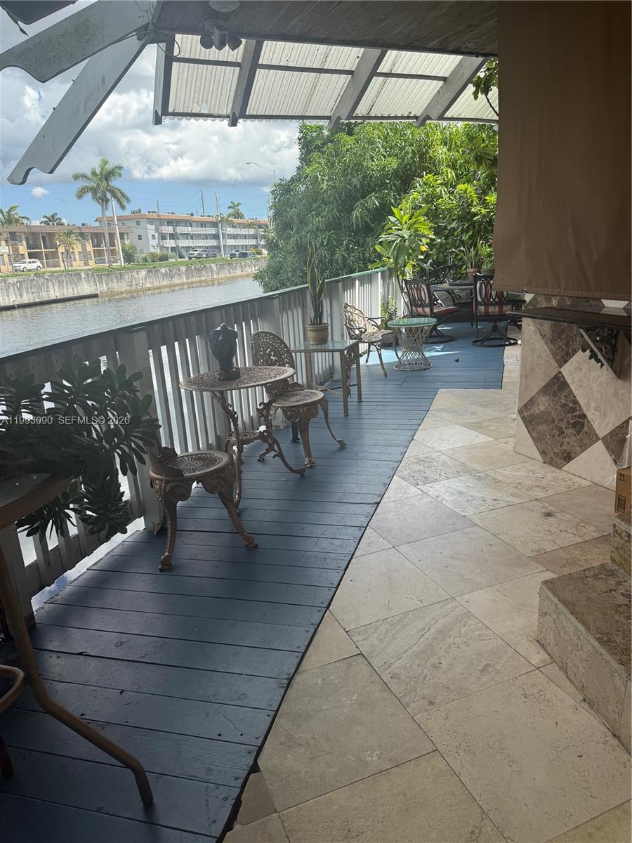 A covered outdoor deck features a tiled floor, wooden decking, and seating overlooking a canal — 7643 NW South River Dr, Medley FL 33166, MEDLEY, FL