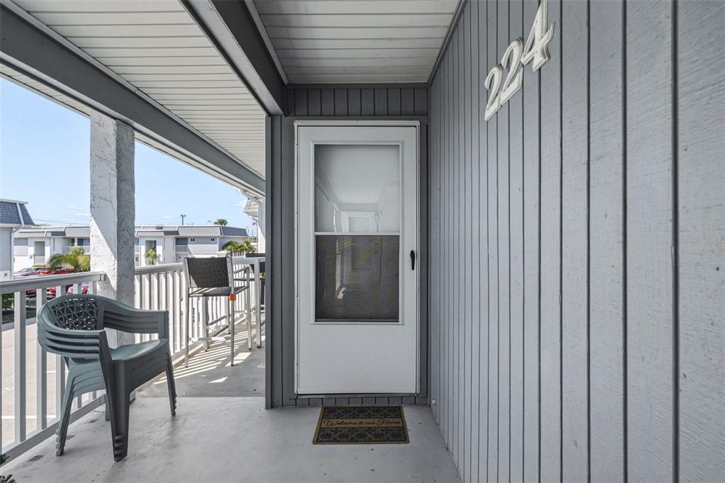 A gray exterior balcony features a white storm door, a house number, and patio furniture — 22375 EDGEWATER DRIVE UNIT 224, PORT CHARLOTTE, FL