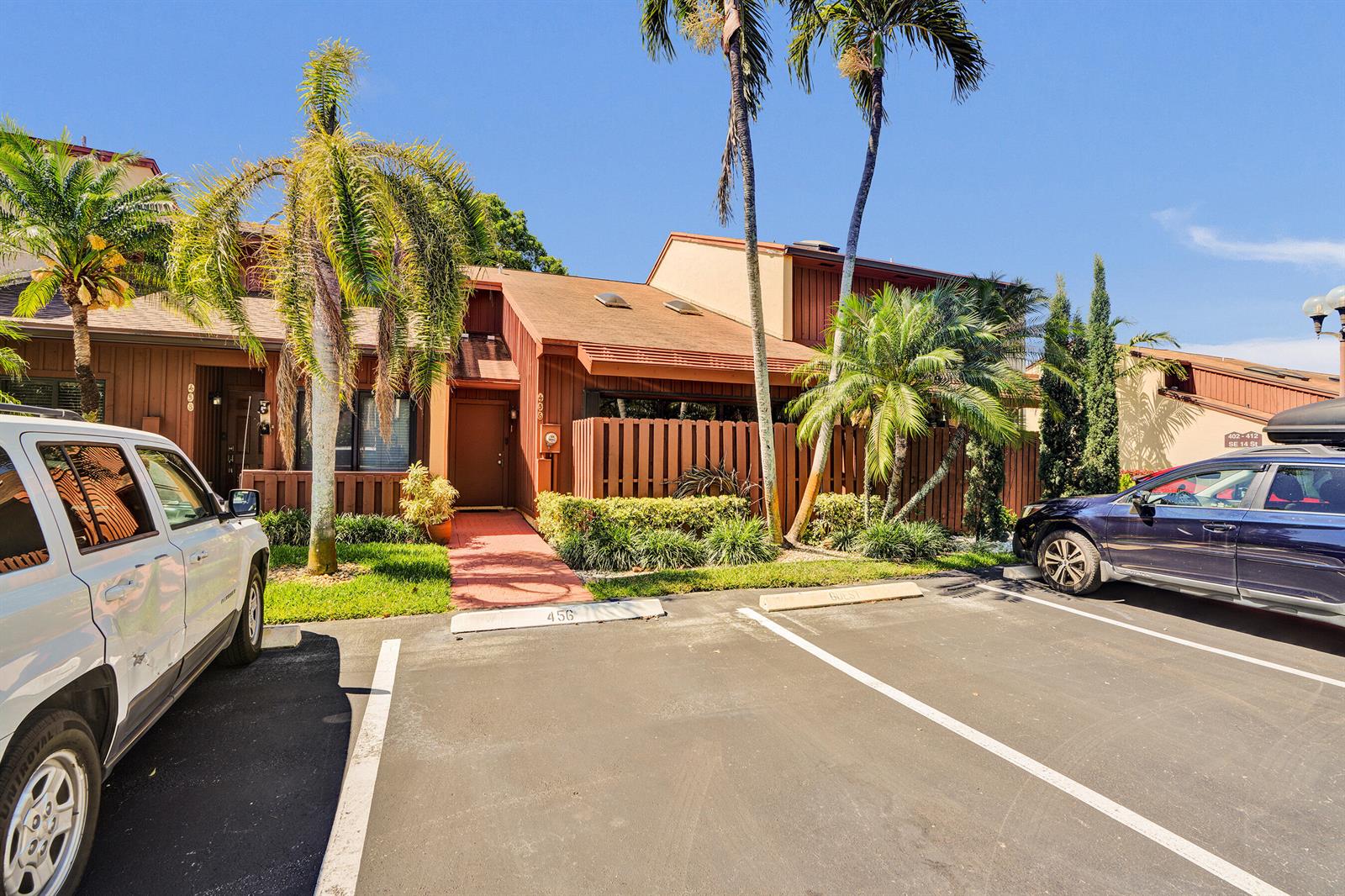 A brown wooden townhouse exterior features a front entrance, palm trees, and a parking lot — 456 SE 14th Street, Dania Beach FL 33004, DANIA BEACH, FL