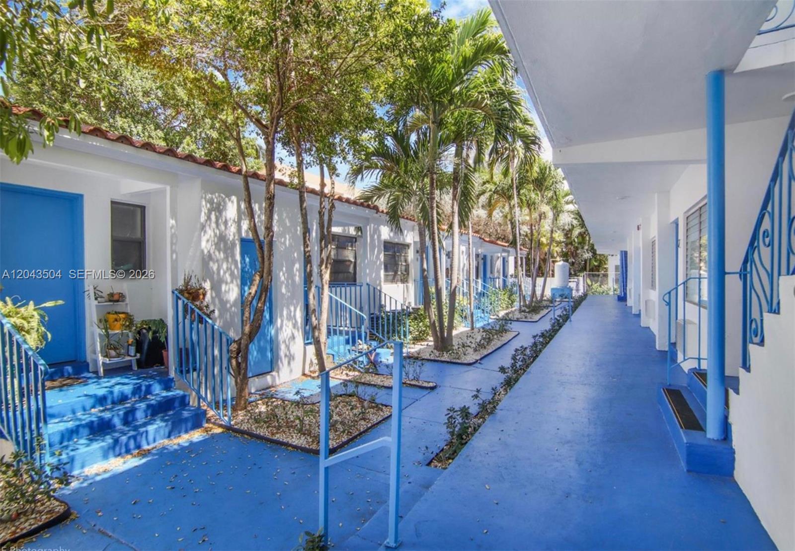 An outdoor walkway with blue painted concrete floors and stairs leads past white apartment units — 7717 Byron Ave, Miami Beach FL 33141, MIAMI BEACH, FL