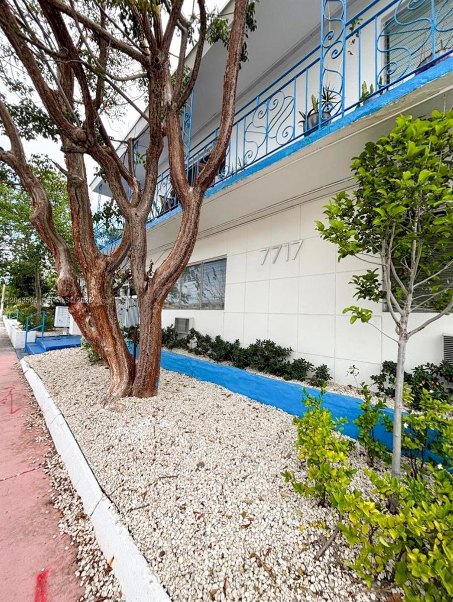 A white apartment building exterior features a blue balcony railing and a gravel garden bed — 7717 Byron Ave, Miami Beach FL 33141, MIAMI BEACH, FL