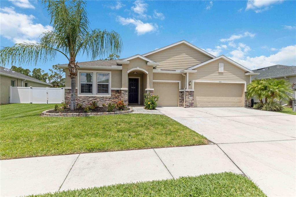 A single-story suburban house with a tan exterior, stone accents, and a two-car garage — 214 TAPA PARISH RUN, BRADENTON, FL