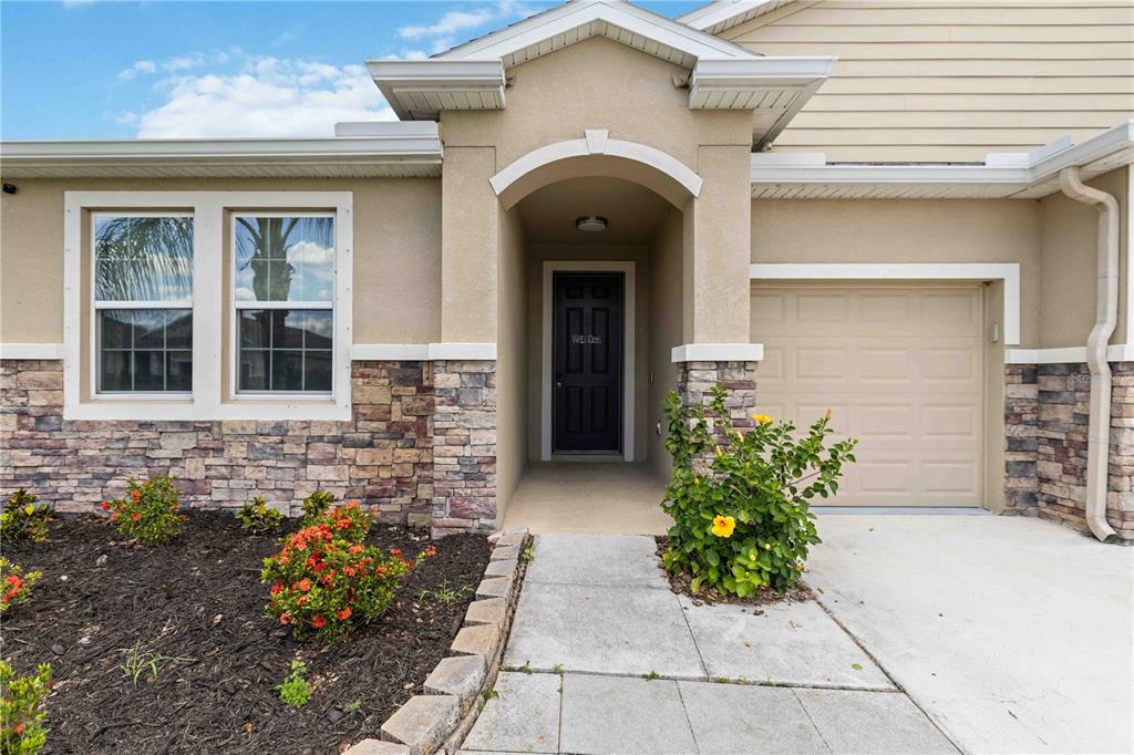 A tan house exterior features a stone facade, a covered entryway, and a concrete driveway — 214 TAPA PARISH RUN, BRADENTON, FL