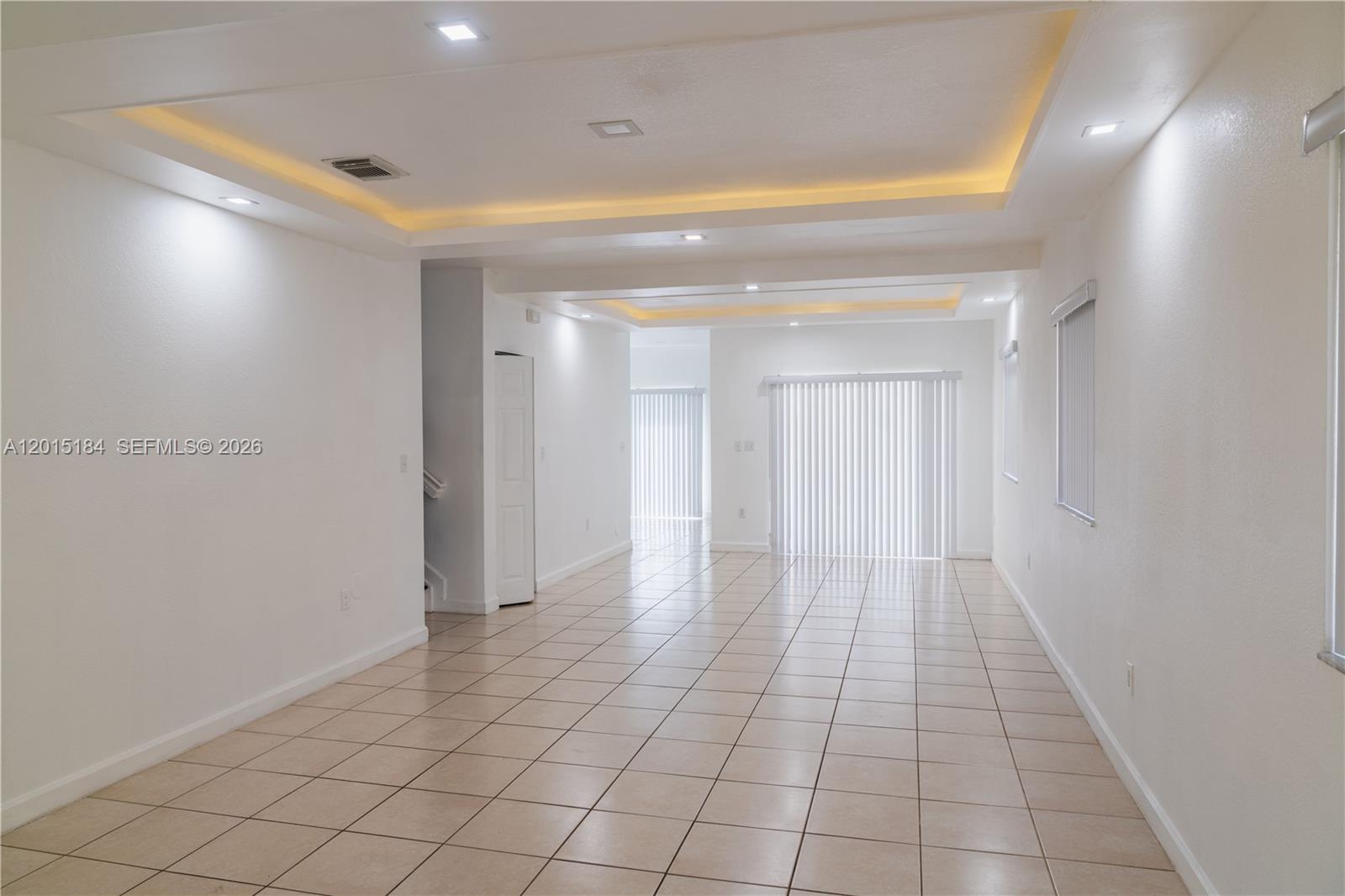 A bright, empty room features white walls, tiled flooring, and a recessed tray ceiling — 379 NE 34th Ave, Homestead FL 33033, HOMESTEAD, FL