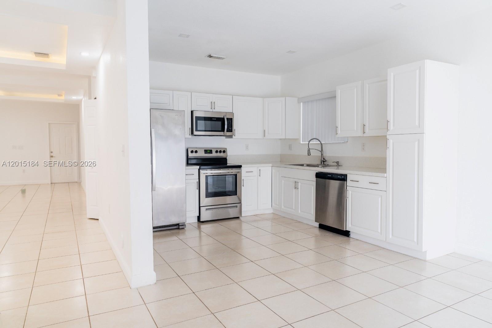 A kitchen features white cabinets, stainless steel appliances, and light-colored tile flooring — 379 NE 34th Ave, Homestead FL 33033, HOMESTEAD, FL