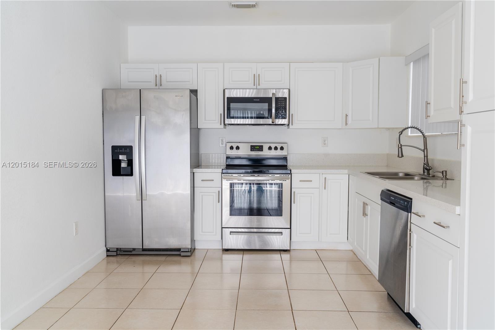 A kitchen features white cabinets, stainless steel appliances, and light-colored tile flooring — 379 NE 34th Ave, Homestead FL 33033, HOMESTEAD, FL