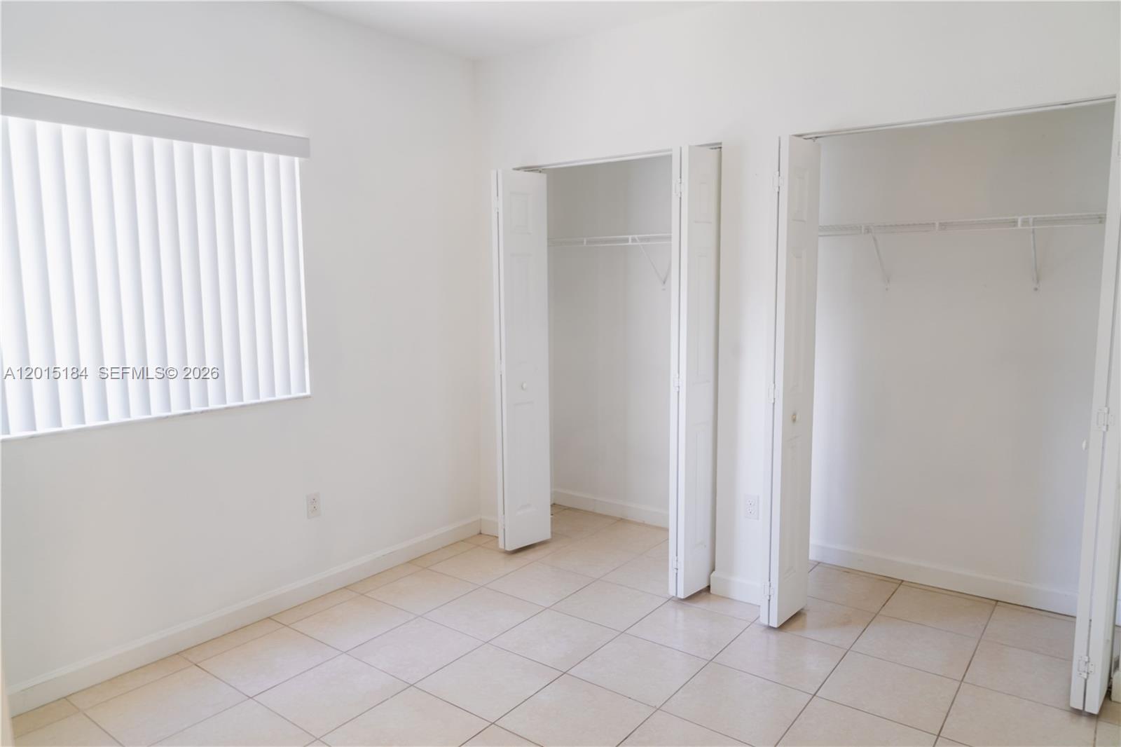 An empty room features white walls, tile flooring, a window with vertical blinds, and two closets — 379 NE 34th Ave, Homestead FL 33033, HOMESTEAD, FL