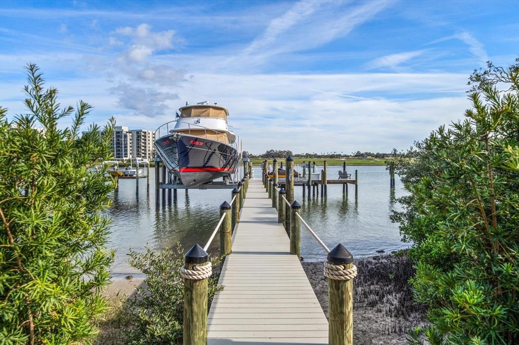 A wooden dock leads to a boat lift holding a large yacht over the water — 430 ST ANDREWS DRIVE, BELLEAIR, FL