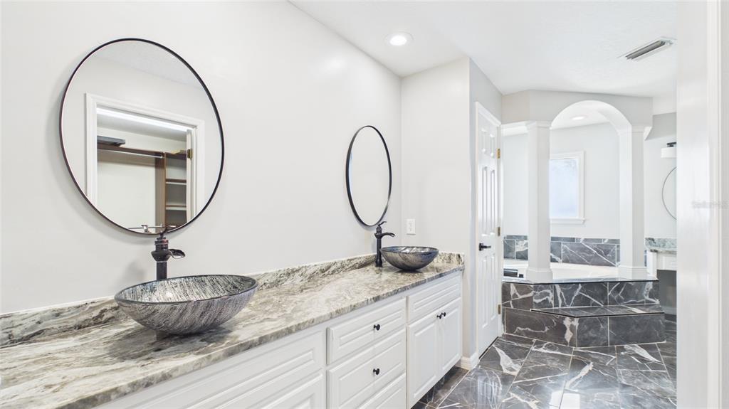 A bathroom features a dual-sink vanity with marble countertops, vessel sinks, and dark-framed mirrors — 315 LANCEOLATE DRIVE, WINTER HAVEN, FL