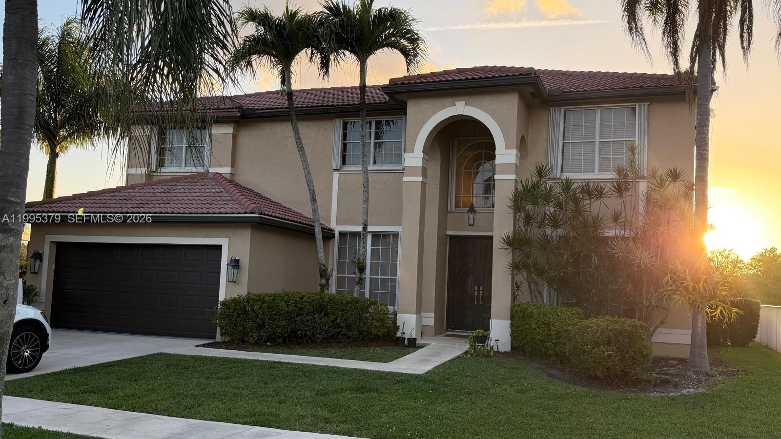 A two-story stucco house with a tile roof, arched entryway, and attached garage at sunset — 2386 SW 183rd Ter, Miramar FL 33029, MIRAMAR, FL