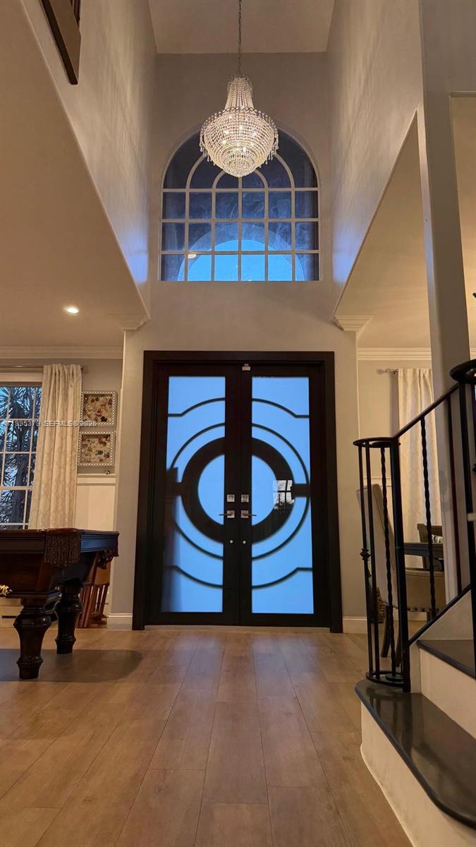 A high-ceilinged foyer features a crystal chandelier, double glass-paneled doors, and hardwood flooring — 2386 SW 183rd Ter, Miramar FL 33029, MIRAMAR, FL