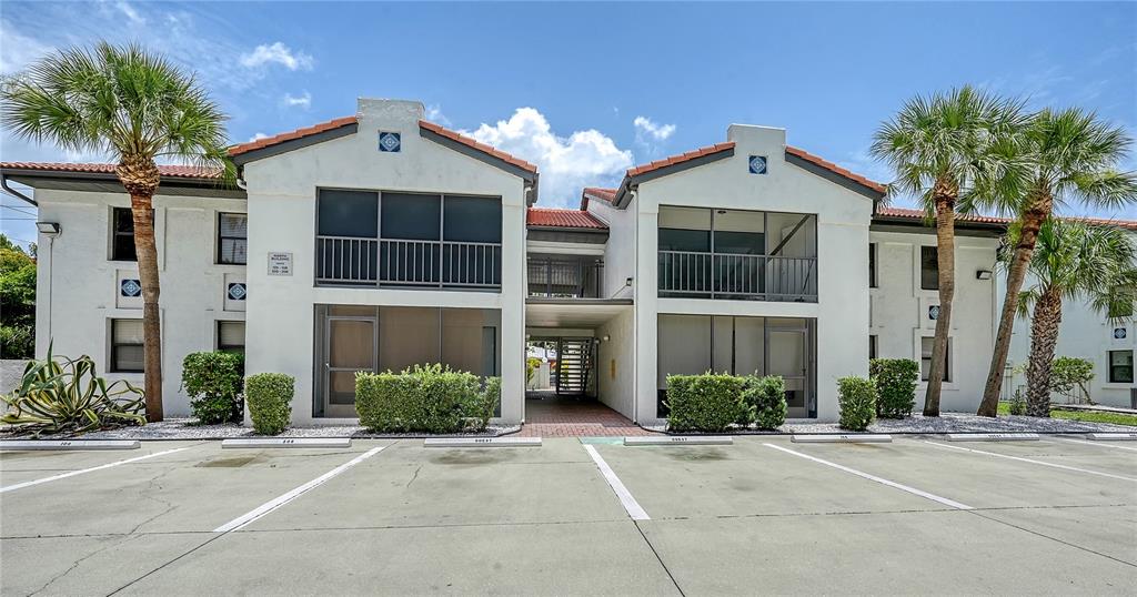 A two-story stucco apartment building features screened balconies, palm trees, and a paved parking lot — 631 N ORANGE AVENUE UNIT 208, SARASOTA, FL