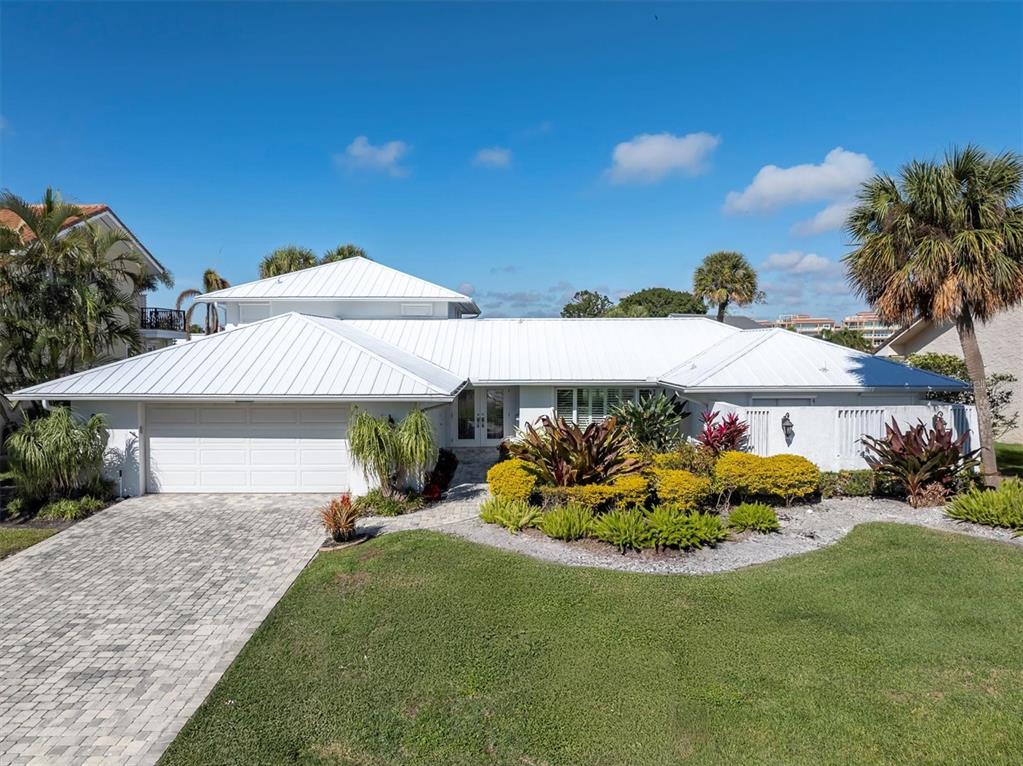 A white house with a metal roof, a paved driveway, and a landscaped front yard — 4935 62ND AVENUE S, ST PETERSBURG, FL