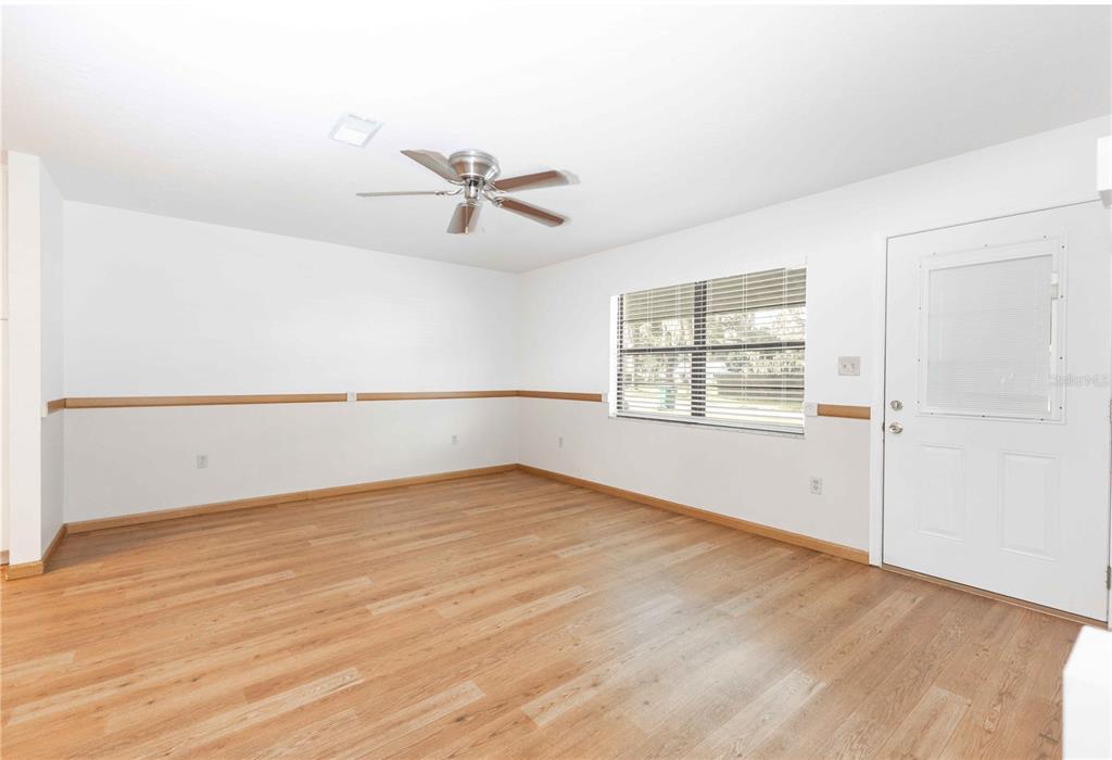 An empty room features light wood-look flooring, white walls with chair rail molding, and a ceiling fan — 301 CURRY STREET, WILDWOOD, FL