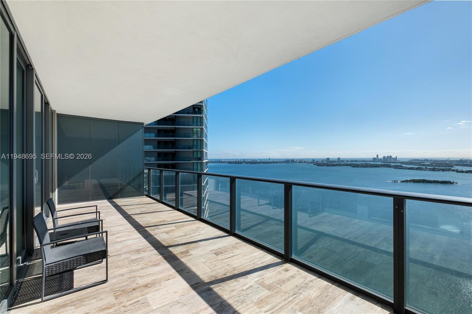 A balcony with wood-look tile flooring, glass railings, and chairs overlooks a bay and city — 650 NE 32nd St # 4306, Miami FL 33137, MIAMI, FL