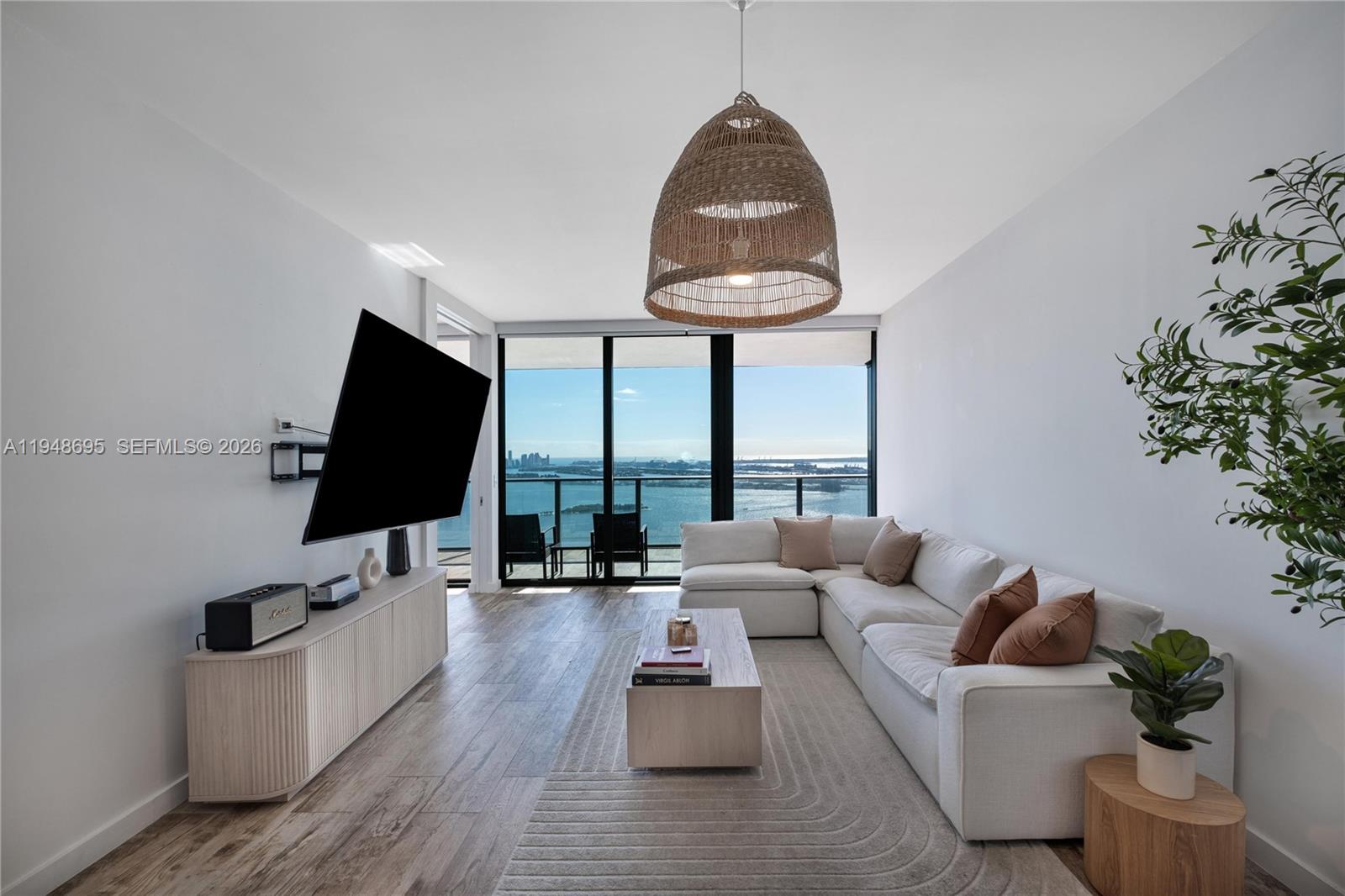 A modern living room features a white sectional sofa, a television, and a waterfront balcony — 650 NE 32nd St # 4306, Miami FL 33137, MIAMI, FL