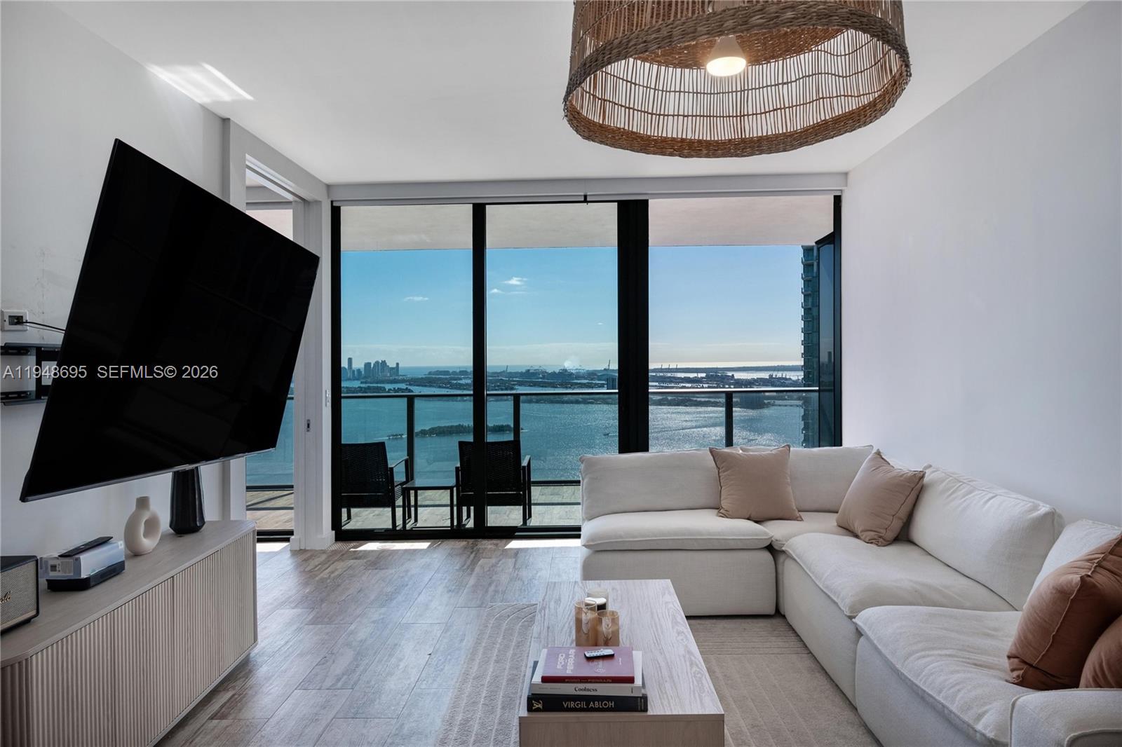A living room features a white sectional sofa, a television, and floor-to-ceiling windows overlooking water — 650 NE 32nd St # 4306, Miami FL 33137, MIAMI, FL