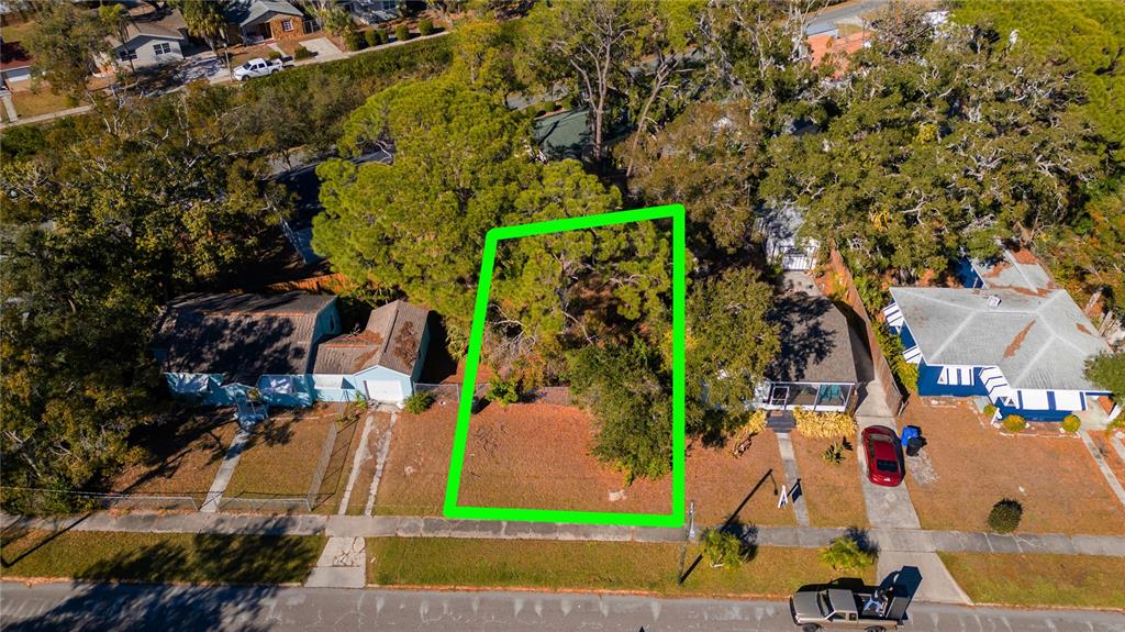 An aerial view shows a vacant, tree-covered residential lot outlined in green between two houses — 26TH AVENUE S, ST PETERSBURG, FL
