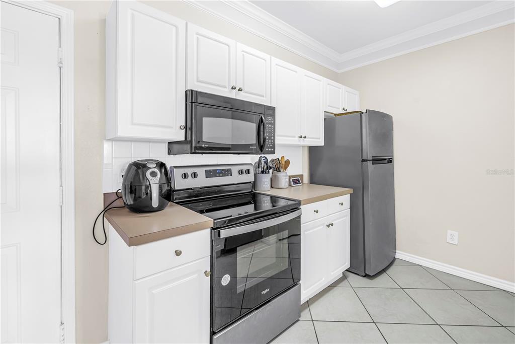 A kitchen features white cabinets, stainless steel appliances, a tan countertop, and light-colored tile flooring — 4333 BAYSIDE VILLAGE DRIVE UNIT 320, TAMPA, FL