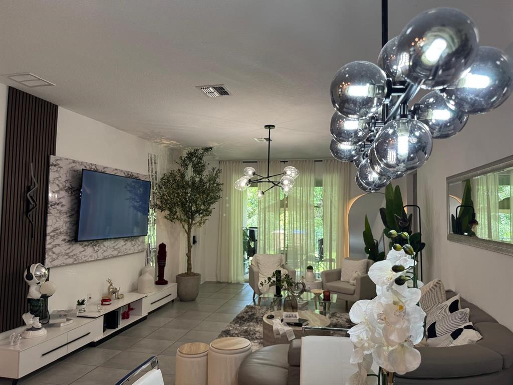 A modern living room features a marble accent wall, a large television, and globe lighting — 4138 BABBLING BROOK WAY, KISSIMMEE, FL