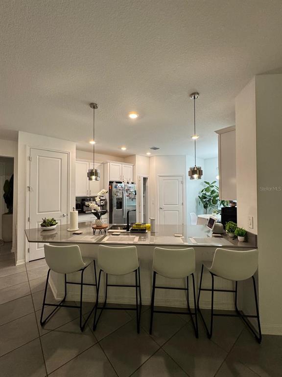 A kitchen features a breakfast bar with four white stools and two pendant lights — 4138 BABBLING BROOK WAY, KISSIMMEE, FL